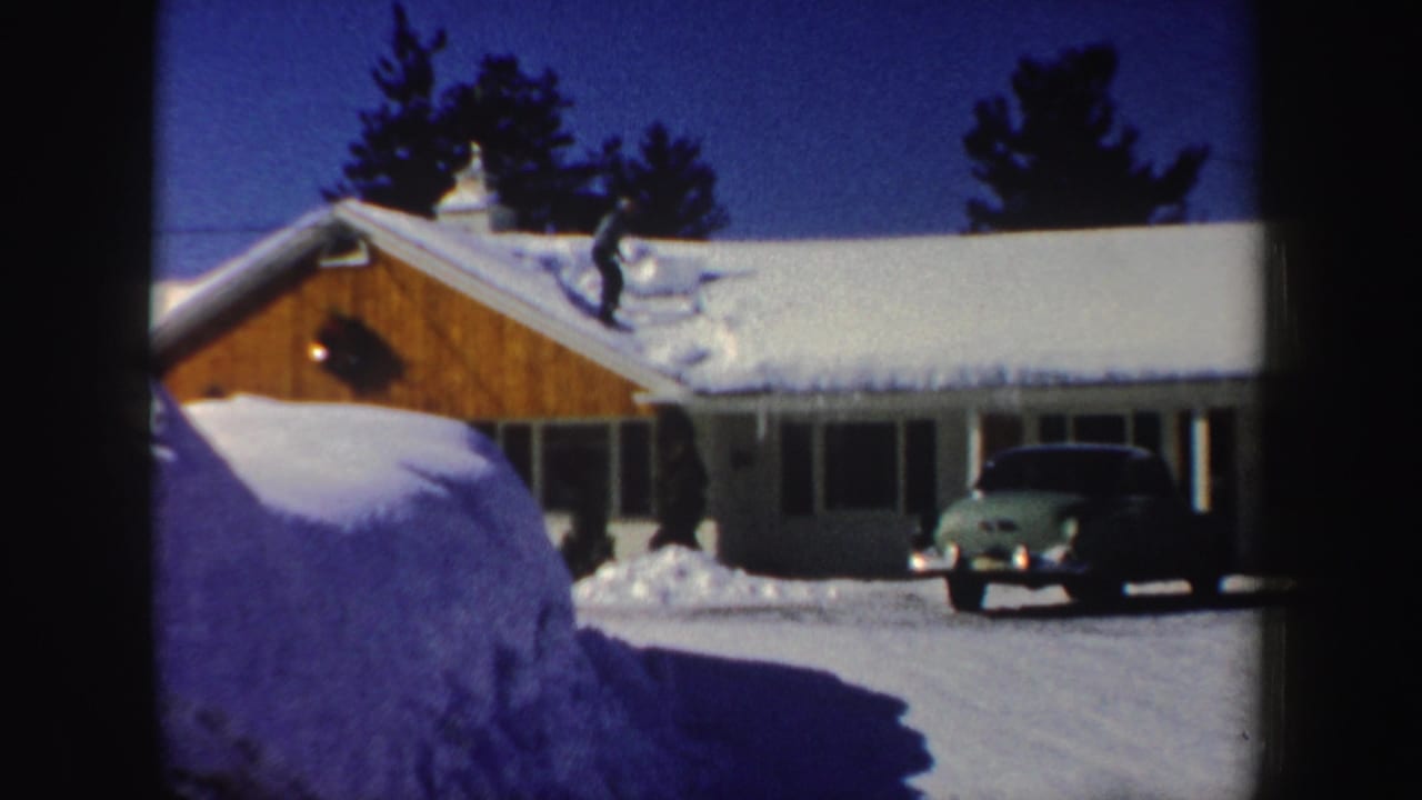 A man clears heavy snow from a sloped residential roof in a 1962 New Hampshire winter home-movie frame.