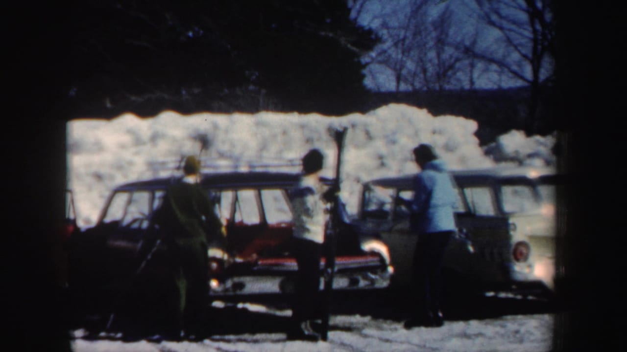Adults in winter clothing stand beside classic station wagons in a snowy New Hampshire clearing, with possible ski gear visible nearby.