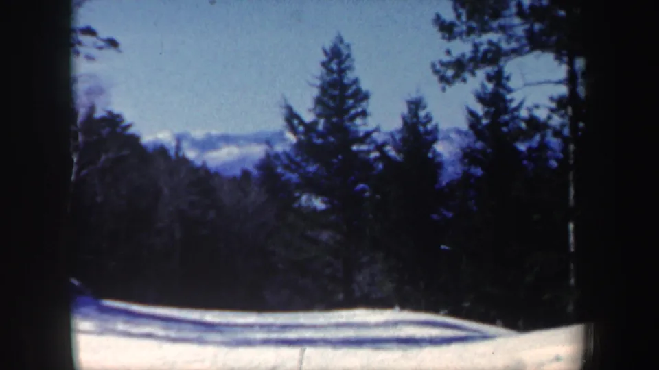 1962 New Hampshire 8mm frame showing snow-covered ground, evergreen trees, and a pale blue winter sky.