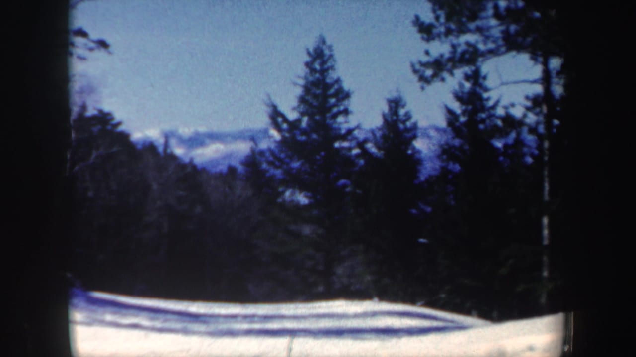 New Hampshire winter home-movie frame with snow, silhouetted evergreens, and visible 8mm frame edges.