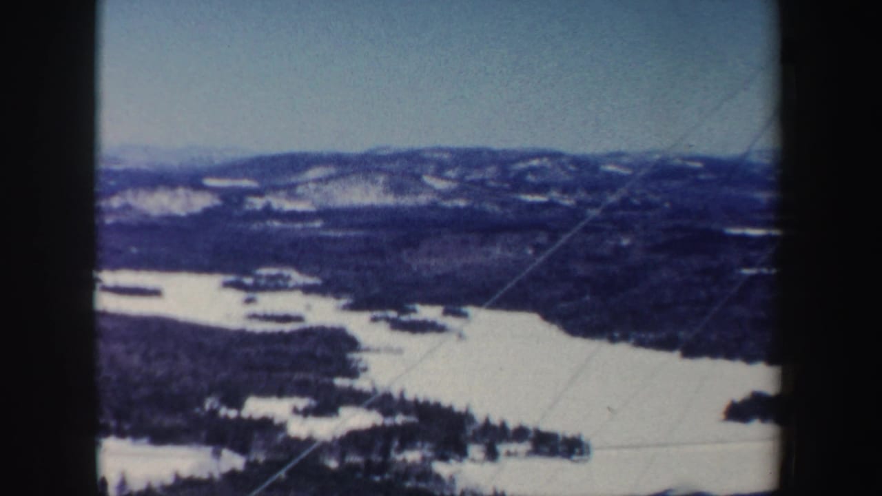 1962 New Hampshire 8mm view looking across a frozen lake or river, wooded shoreline, and snow-dusted hills.
