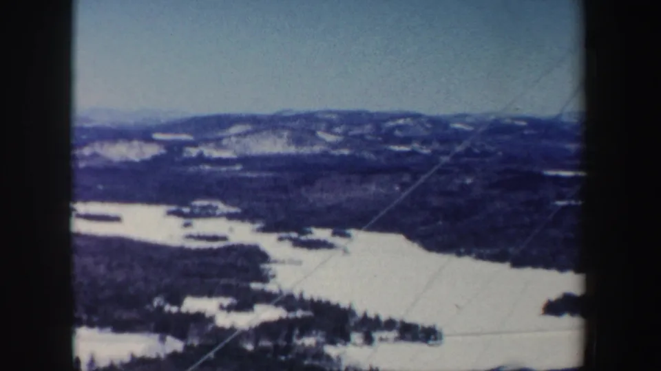 1962 New Hampshire 8mm view looking across a frozen lake or river, wooded shoreline, and snow-dusted hills.