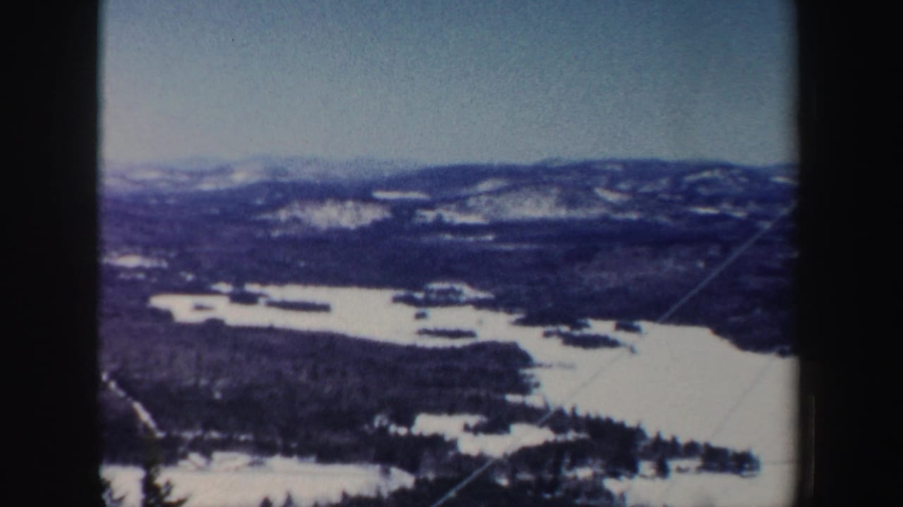 New Hampshire winter landscape frame with frozen water, dark woods, snowy hills, and soft faded 8mm color.