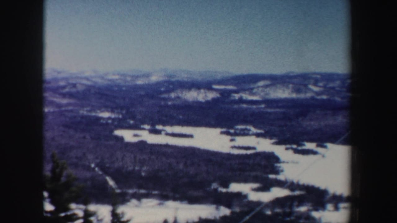 Snowy mountain ridges and frozen lakes seen from a high overlook with dark film borders.