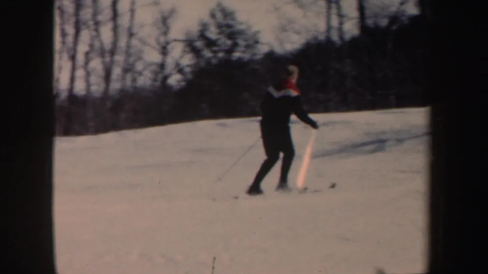 A lone skier in dark clothing with a red-and-white collar moves across a snowy New Hampshire slope in 1962 home-movie footage.