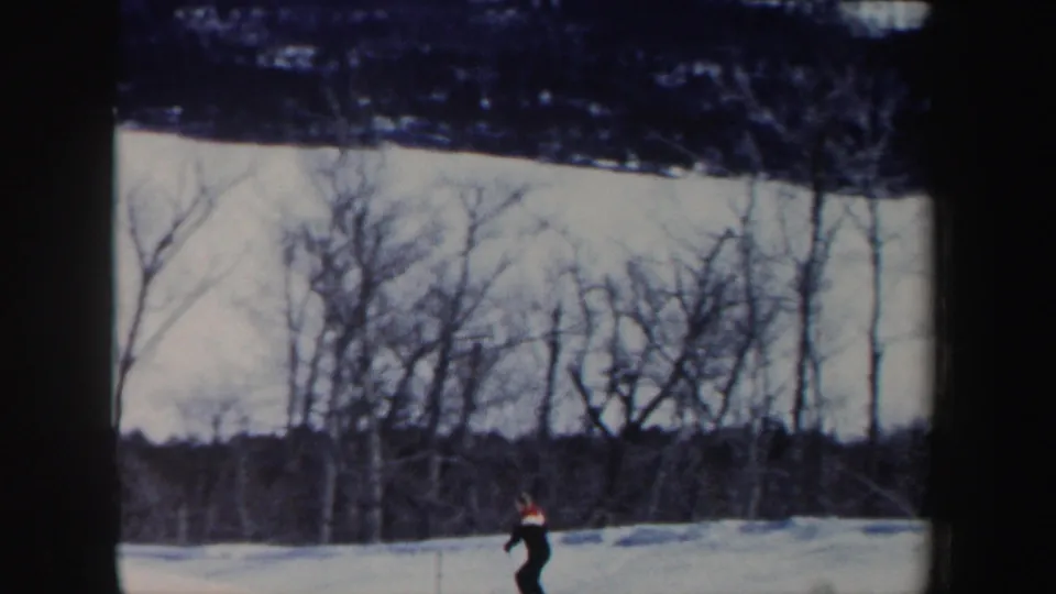 A small figure in a dark ski outfit descends a snowy New Hampshire slope, with winter trees filling the background.