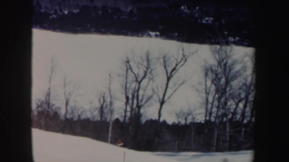 1962 New Hampshire home-movie frame with a distant skier on a snowy hill beneath leafless trees.