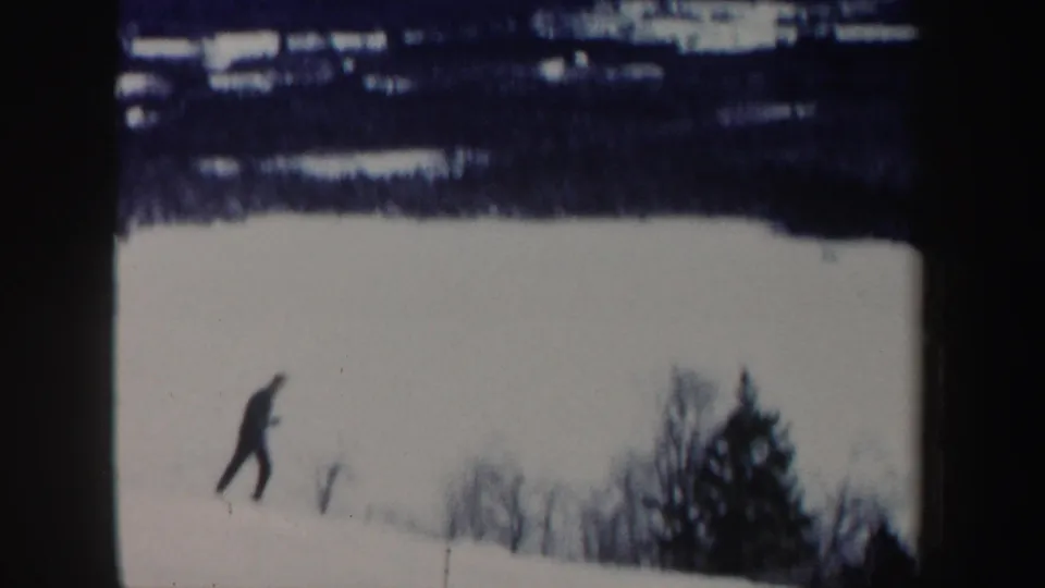 A distant man in dark clothing skis downhill on a snowy New Hampshire slope in 1962 home-movie footage.