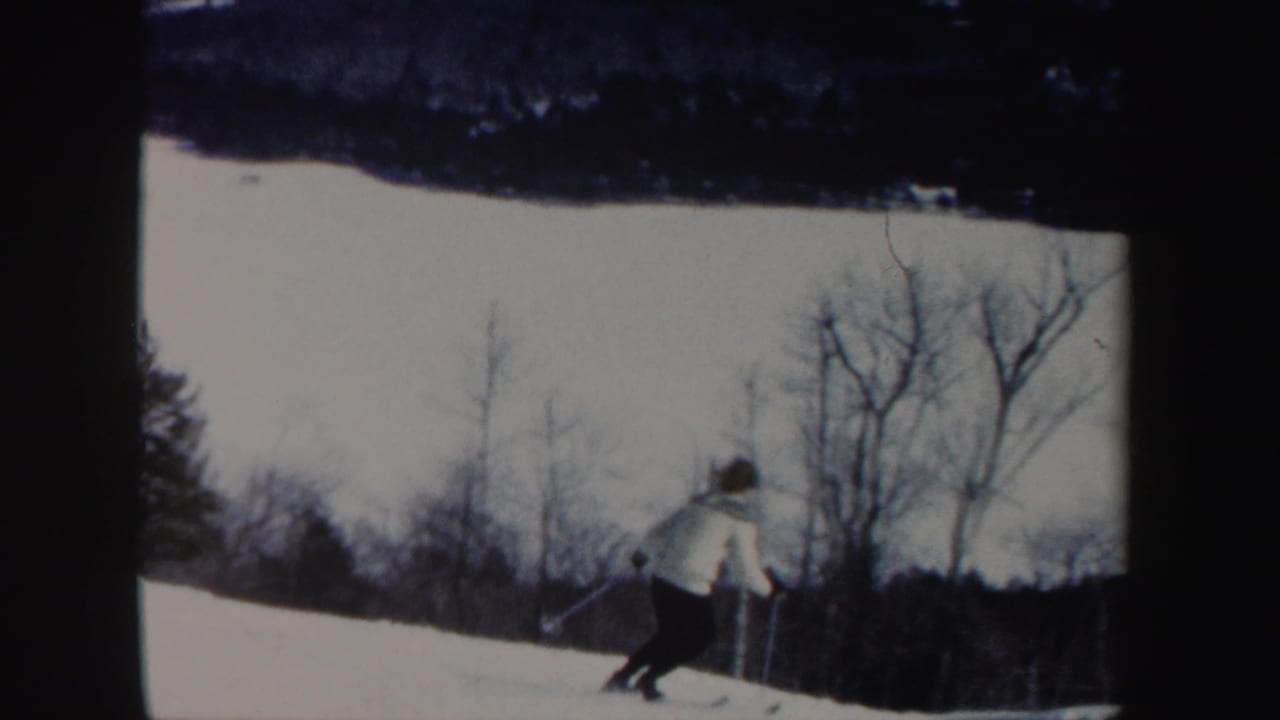 Woman in a white coat skiing down a snowy slope near bare trees.