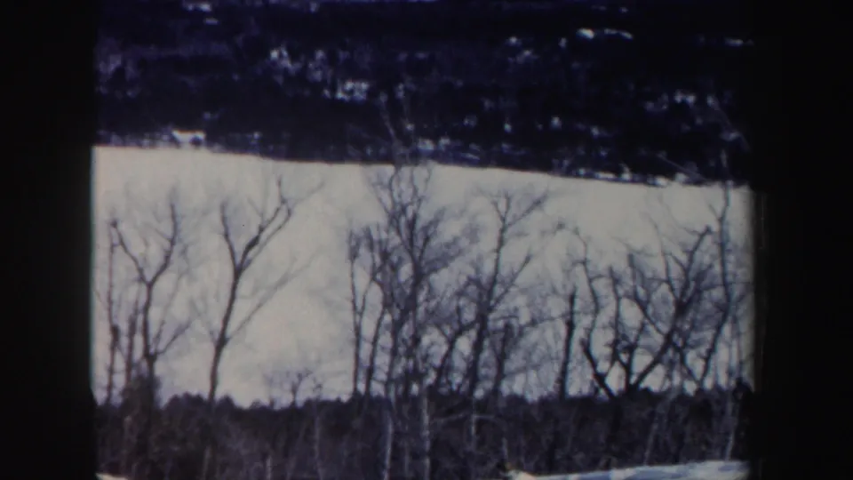 Final 8mm frame shows the skier nearly leaving view below a snowy slope and winter tree line in New Hampshire.