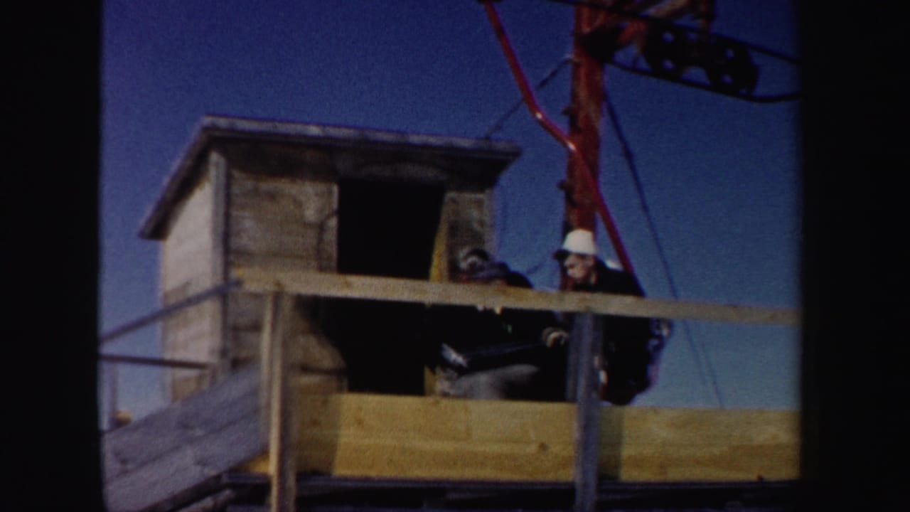 Workers in hard hats stand beside a wooden ski-lift station.