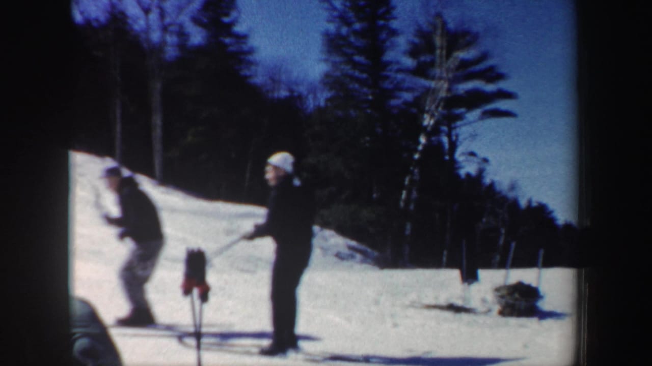 1962 New Hampshire home-movie frame showing two skiers on snow near trees, with soft focus and visible 8mm film borders.