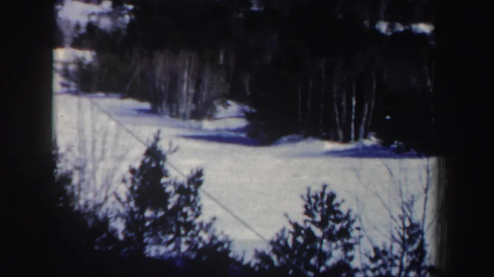 New Hampshire winter slope seen on 8mm film, with snow, surrounding trees, and a diagonal rope or cable crossing the frame.