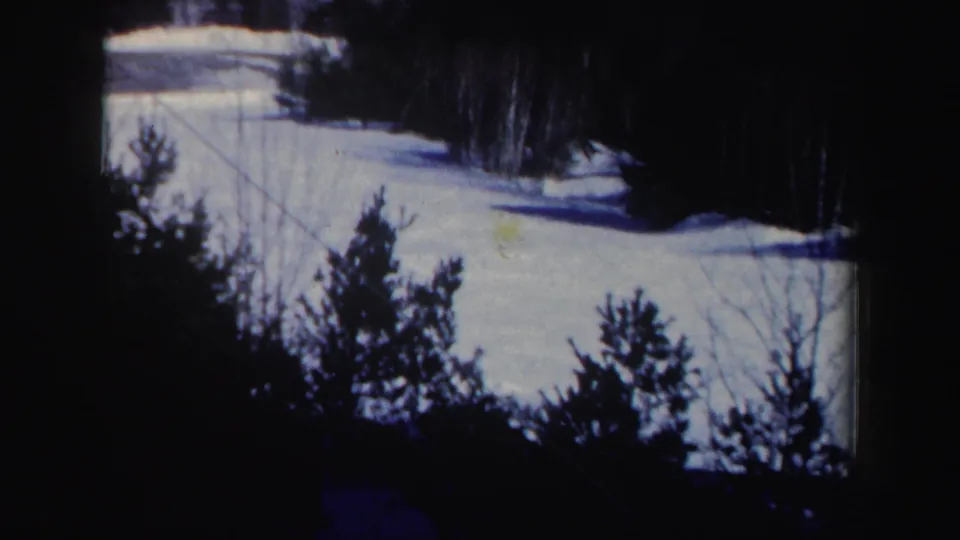1962 New Hampshire home-movie view of a snowy ski slope with dark evergreens, bare trees, and a diagonal line across the foreground.