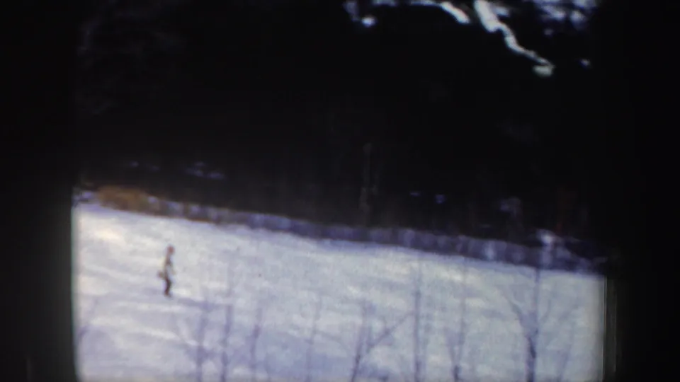 A distant skier descends a snowy 1962 New Hampshire slope, with leafless brush and a dark treeline visible in the frame.