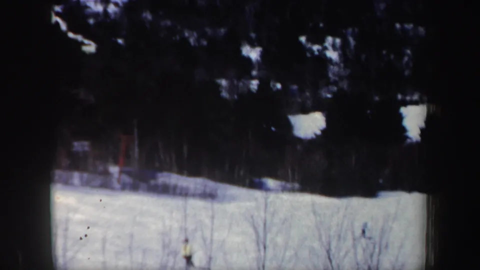 1962 New Hampshire home-movie frame with a small skier on a bright snow-covered slope below a dark tree line.
