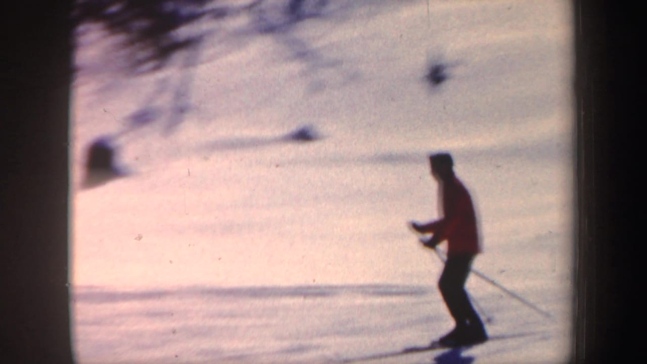 Skier in a red jacket gliding across a bright snowy slope with poles.