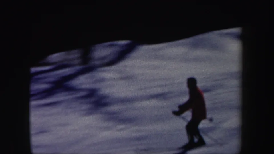 Home-movie frame from 1962 New Hampshire showing a red-jacketed skier as a dark figure on shaded snow.