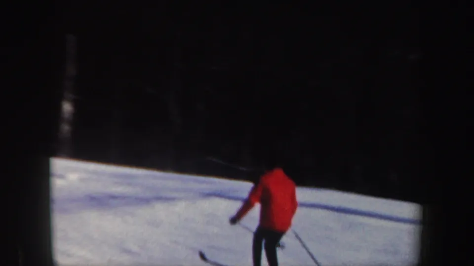The adult skier appears lower on the slope, with red jacket, dark pants, poles, and 8mm frame shadows visible.