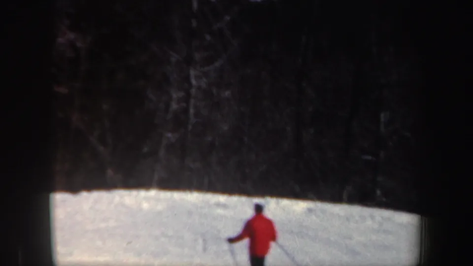A smaller view of the red-jacketed skier shows the snowy slope with dark trees or wooded background above.