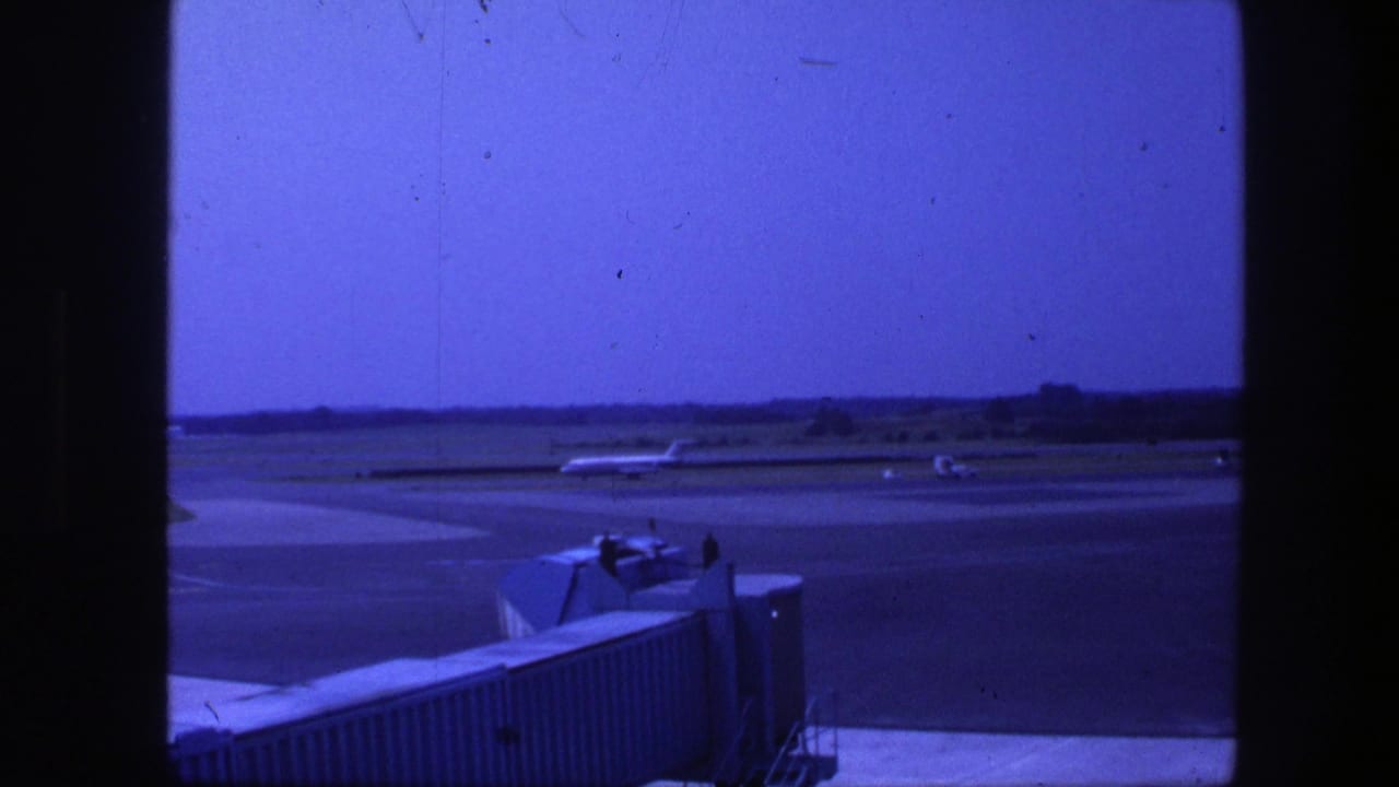 1975 Copenhagen airport terminal view showing a jet bridge in the foreground and aircraft on the tarmac beyond.