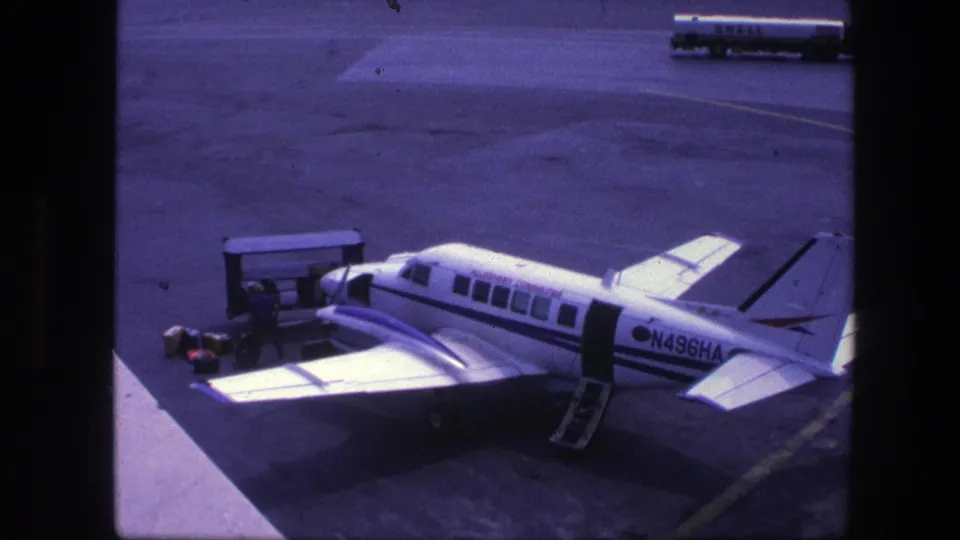 Ground crew appear to handle luggage or service equipment beside aircraft N496HA at Copenhagen airport in 1975, with a Shell tanker behind.