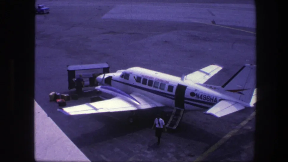 1975 Copenhagen airport footage shows a man walking near a small commuter aircraft while ground equipment stands beside the wing.