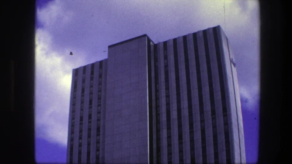 1975 Copenhagen frame of the office building during the pan, showing the upper facade, dark window bands, and bright clouds.