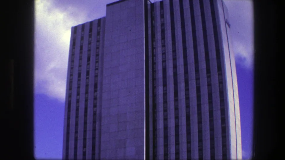 Final 1975 Copenhagen frame showing the high-rise office facade near the edge of the 8mm frame with clouds behind it.
