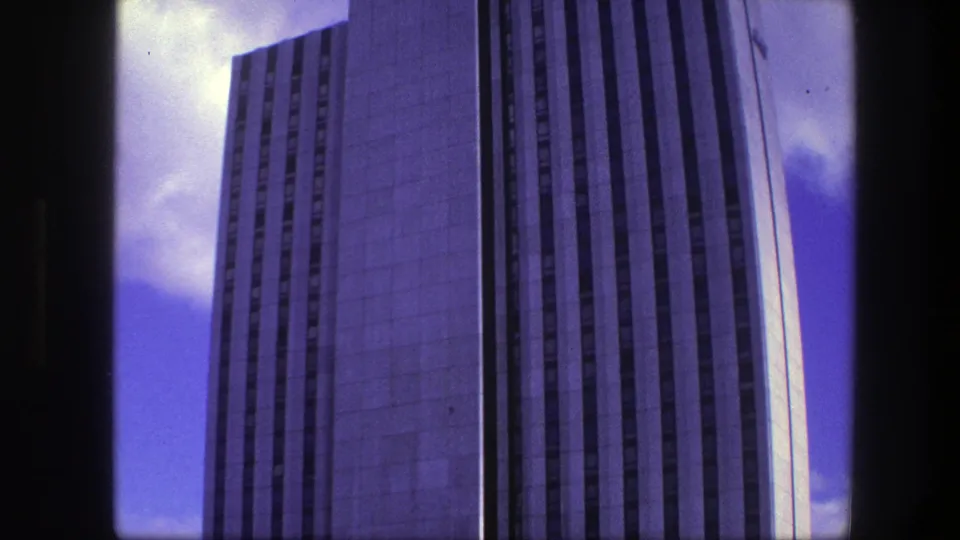 1975 Copenhagen 8mm frame showing the upper portion of a tall concrete high-rise with vertical window bands and blue sky.