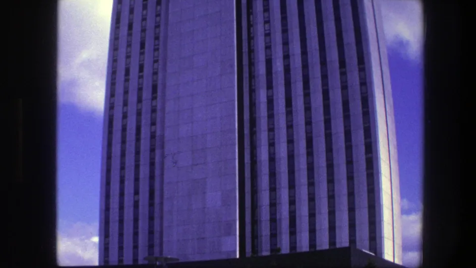 1975 Copenhagen 8mm view of a tall concrete tower facade, filmed upward with dark gate edges and blue sky visible.
