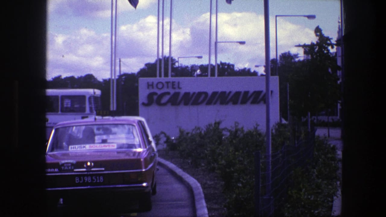Red taxi parked before a Hotel Scandinavia sign with a bus and flagpoles behind it.