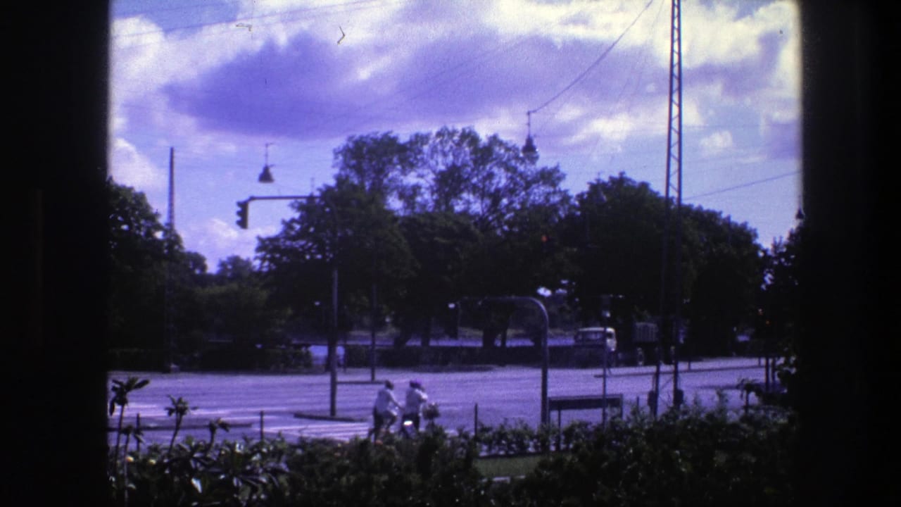 Two cyclists pass near the foreground while a car and truck move along the road behind them.
