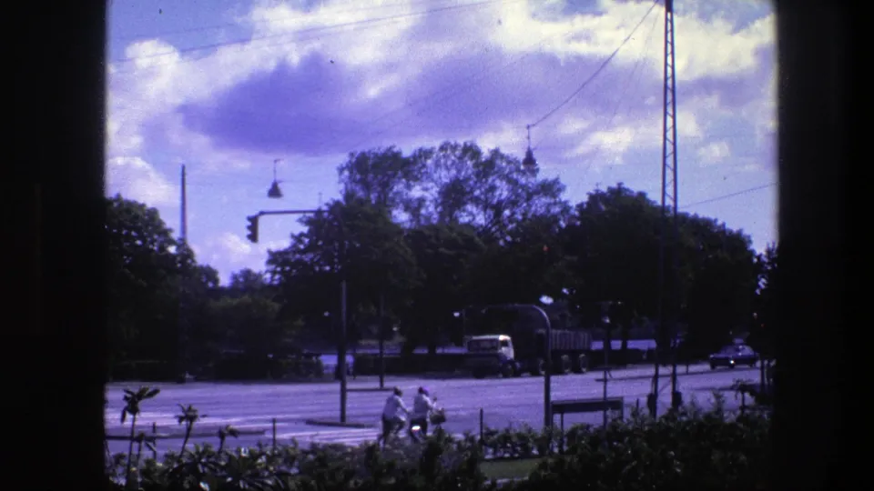 Copenhagen street traffic in 1975 with cyclists at the lower edge, a truck, a small car, wires, trees, and a dark framing edge.