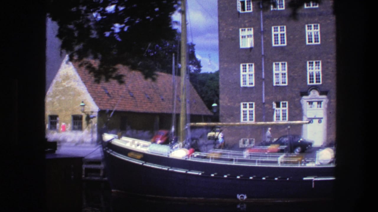 Dark moored boat beside a brick waterfront building and red-tiled roof structure.