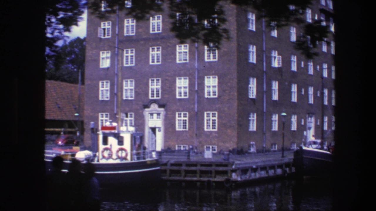 Brick waterfront building beside a canal with a small moored boat and life rings.