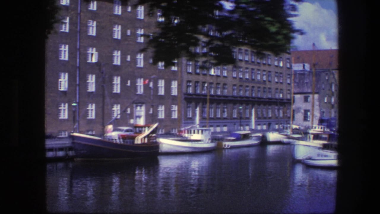 1975 Copenhagen canal view with small boats moored along brick residential buildings, seen in soft 8mm color.