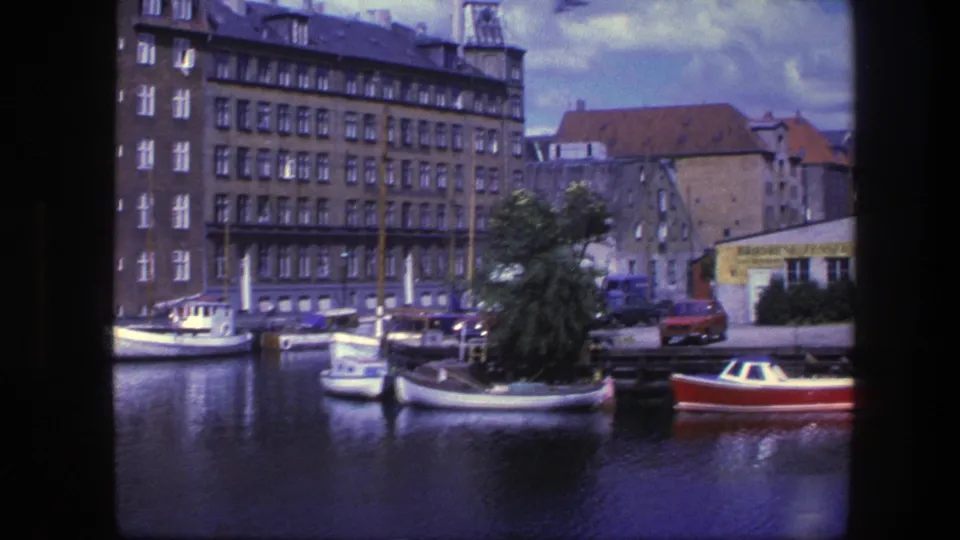 Copenhagen canal footage from 1975 showing boats, brick buildings, a red car, and a partially readable yellow sign near the quay.