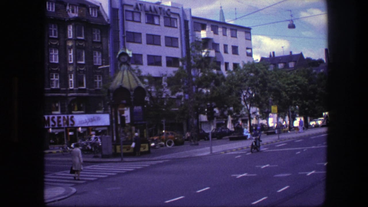 1975 Copenhagen street view with a zebra crossing, pedestrians, a motorcyclist, vintage cars, and a building marked ATLANTIC.