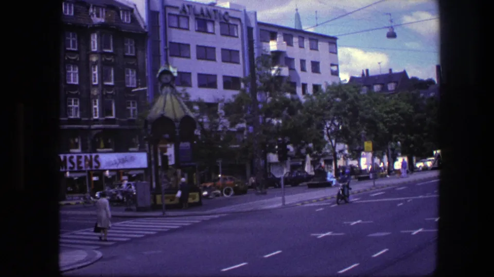 1975 Copenhagen street view with a zebra crossing, pedestrians, a motorcyclist, vintage cars, and a building marked ATLANTIC.