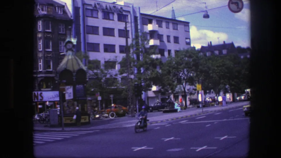 Copenhagen avenue scene from 1975 showing a motorcyclist near the crossing, pedestrians by shops, cars, and ATLANTIC signage.