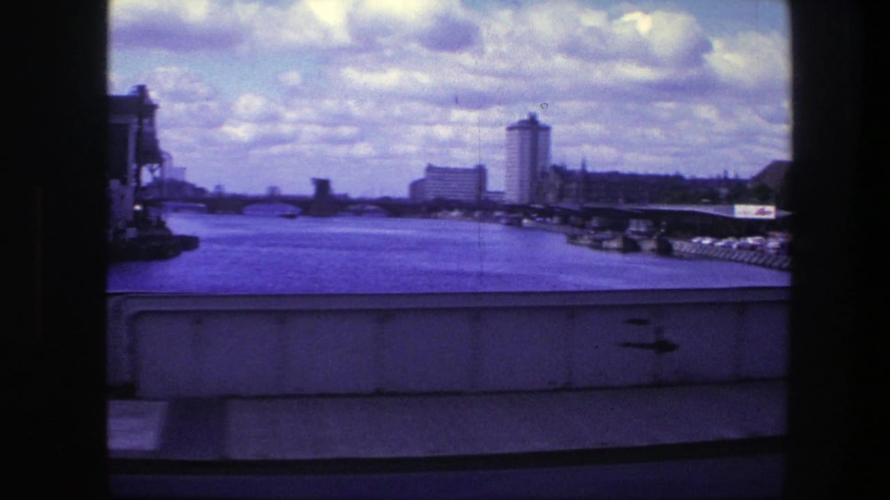 Waterfront view with canal or river, bridge or quay edge, tall buildings, and clouded sky.