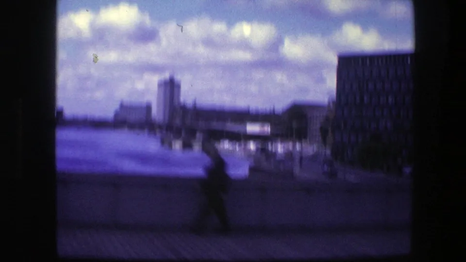 1975 Copenhagen waterfront view with an incidental silhouetted pedestrian, water, distant city buildings, and a dark building along the right edge.