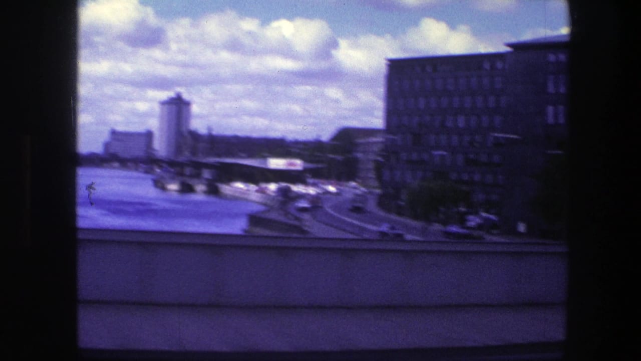 Drive-by view of a city road beside water with buildings and traffic.