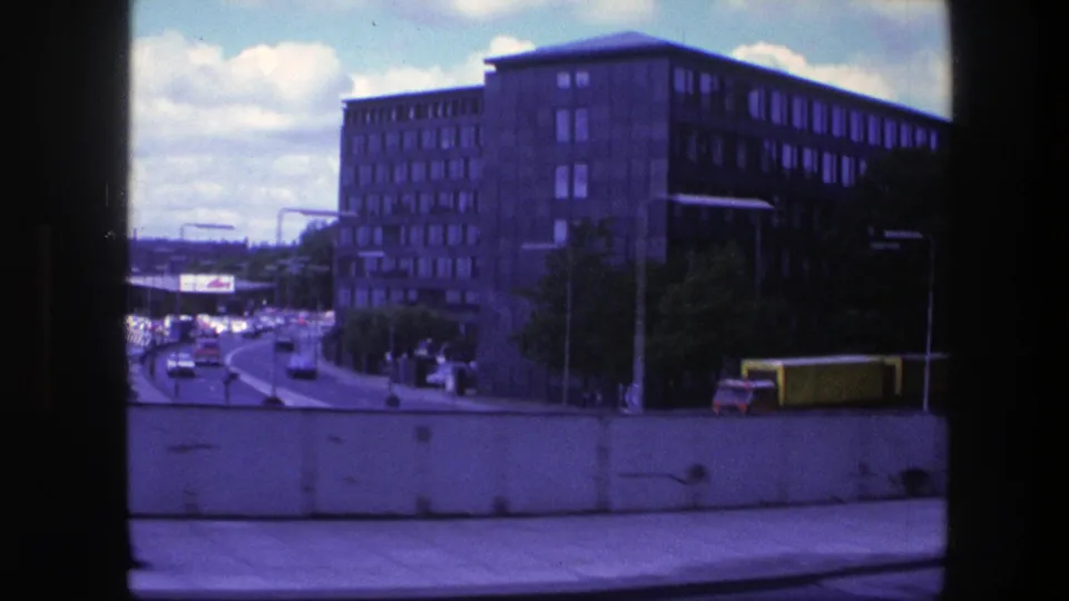 1975 Copenhagen street scene with traffic, a yellow truck, large office-like buildings, street lamps, and a purple 8mm color cast.