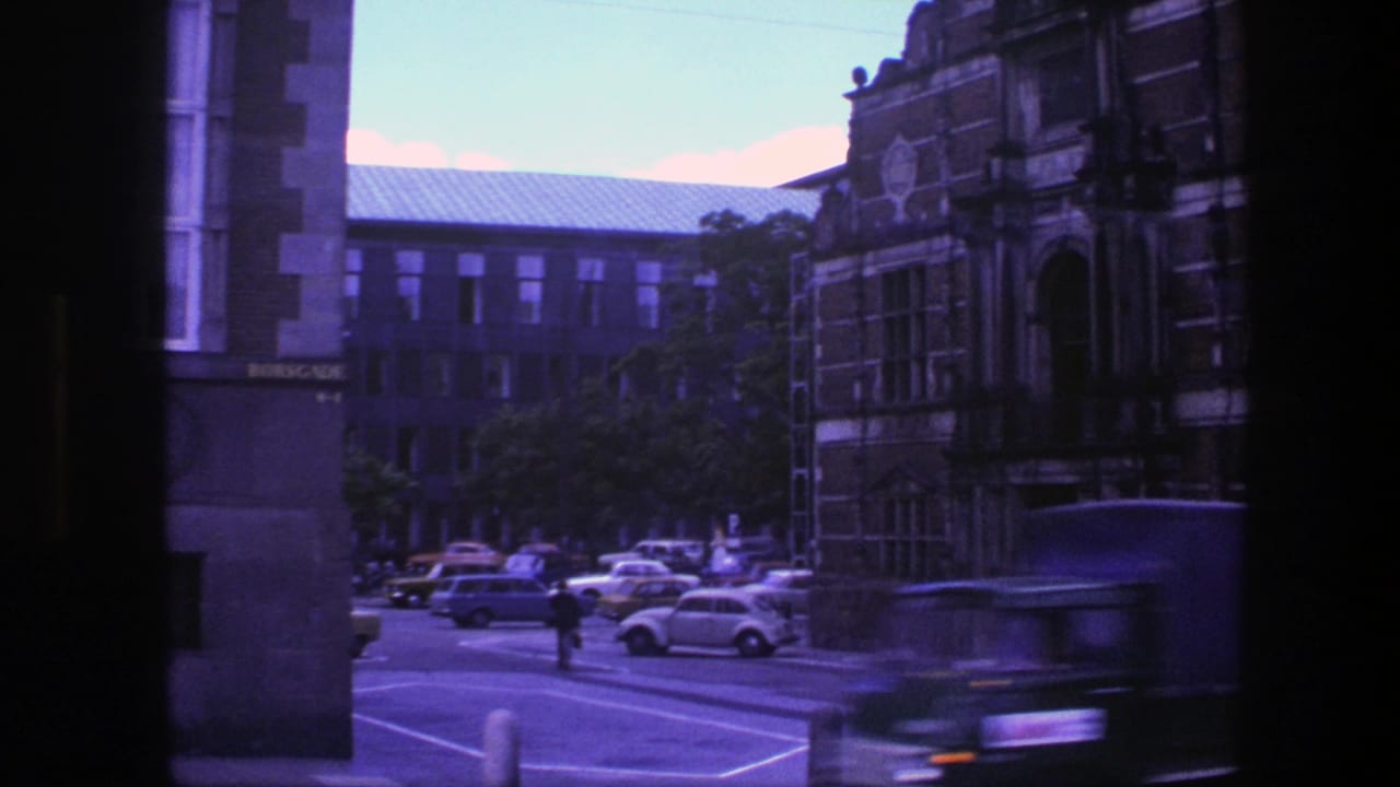 Street view of ornate Copenhagen buildings with parked cars and a small car near the curb.