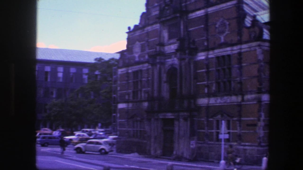 Similar street view of historic buildings, parked cars, and a pedestrian crossing the road.
