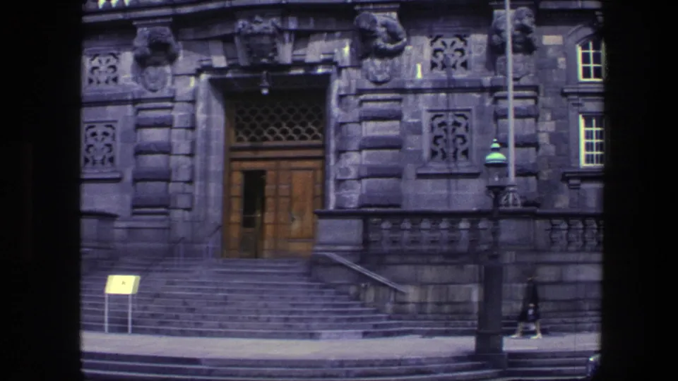 Street-level 8mm view of a grand Copenhagen stone entrance with broad steps, carved facade details, a wooden door, and a pedestrian nearby.