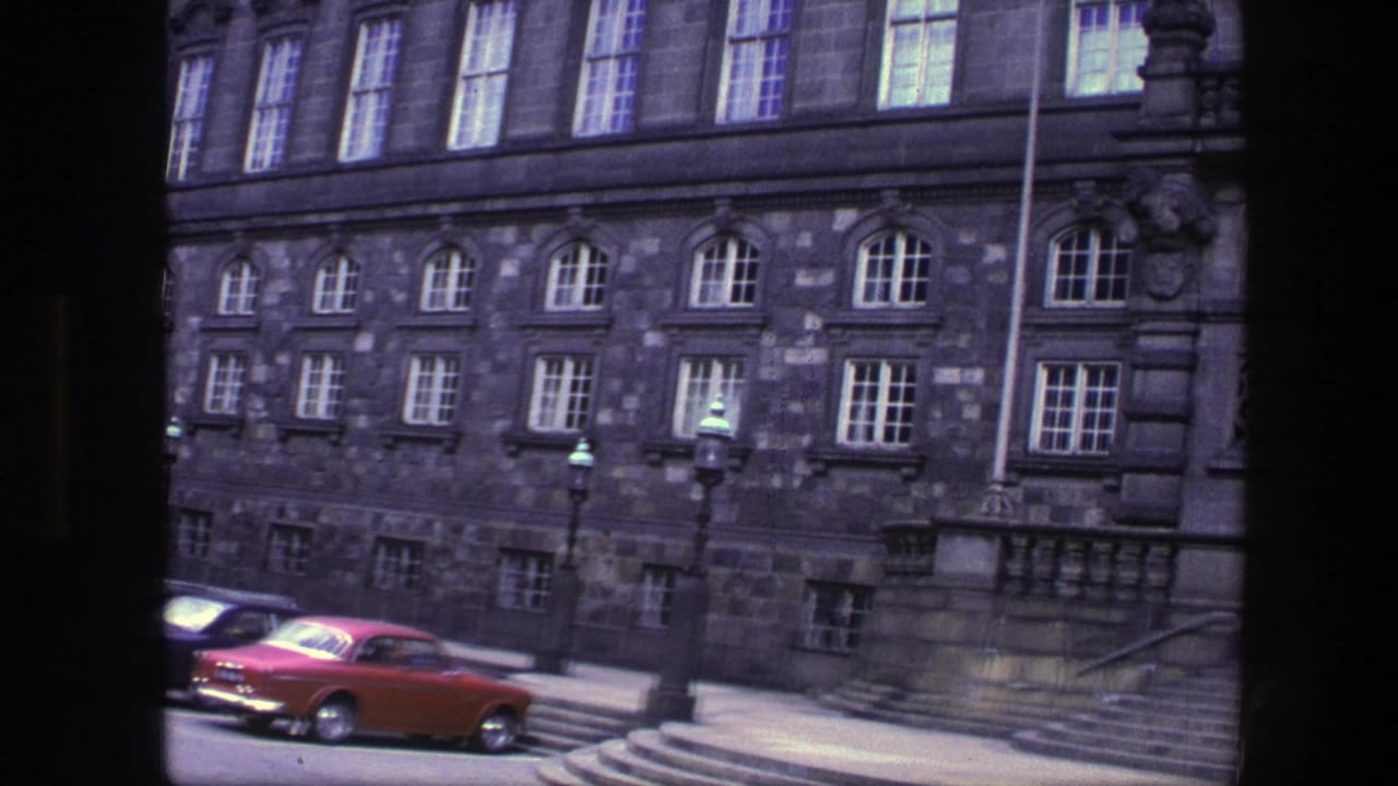 Red car parked beside steps in front of a large stone building.