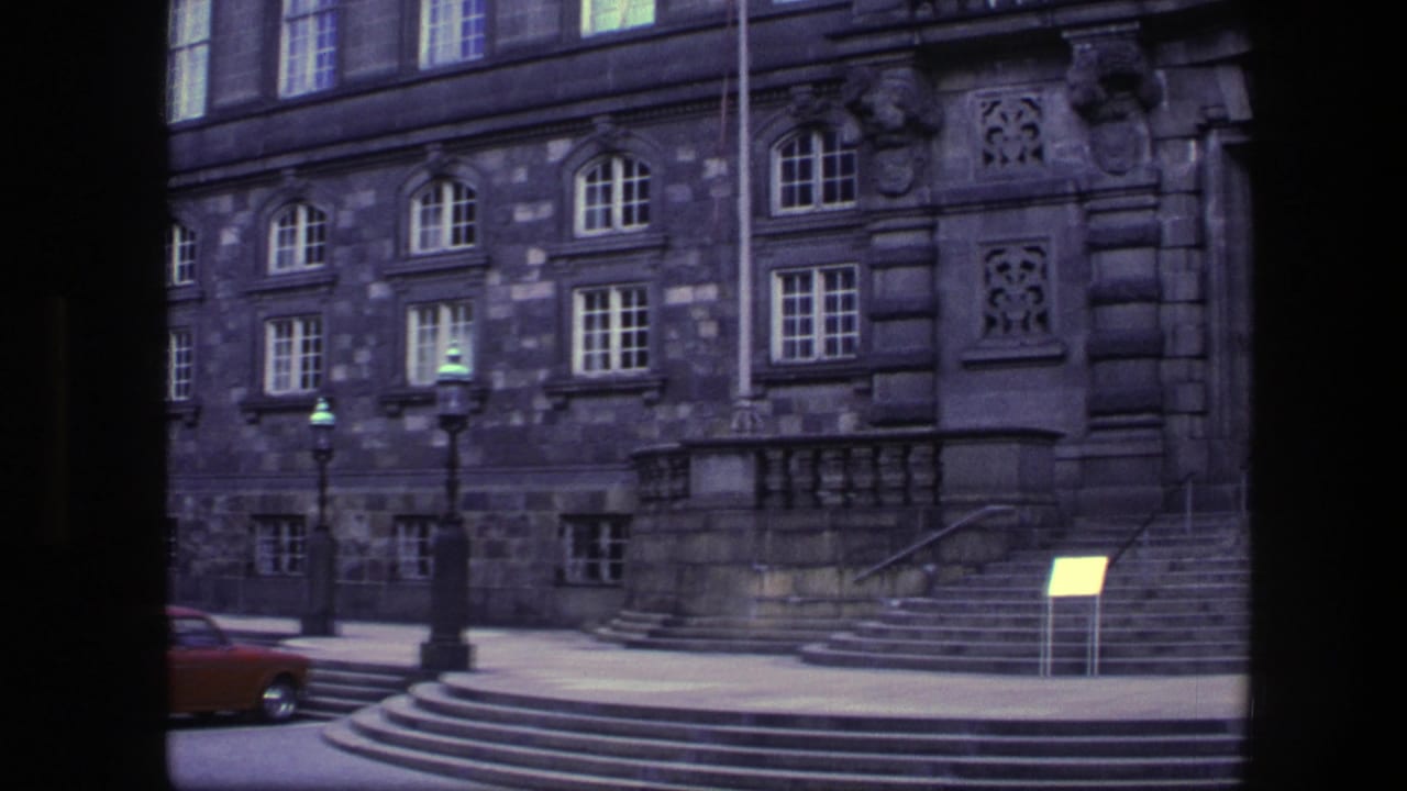 Stone facade with arched windows, steps, lampposts, and a small signboard.
